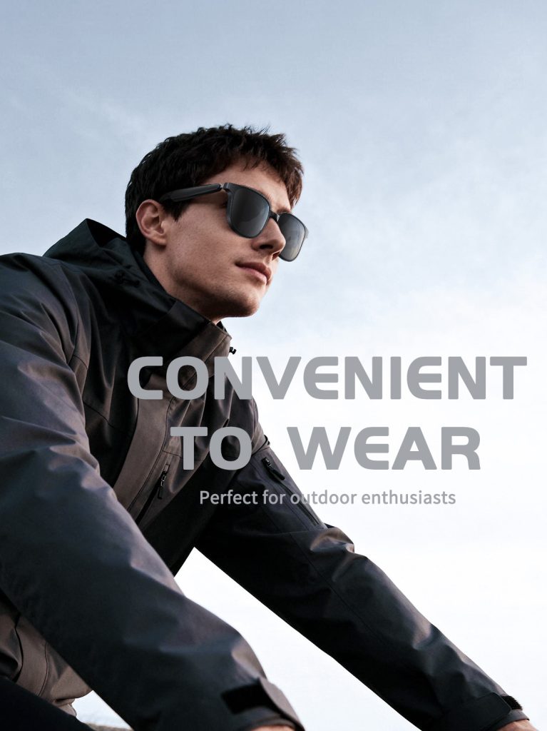 Black open-ear Bluetooth audio sunglasses worn by a person in a dark jacket