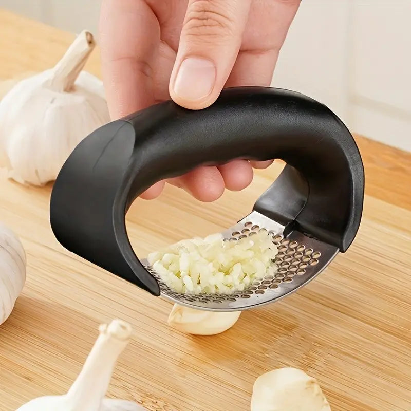Hand holding a black garlic press over a cutting board with minced garlic visible