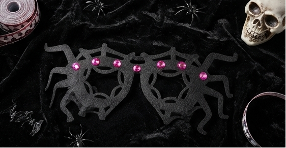 Spider web glasses lying on dark fabric, black frame with pink gem accents
