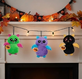 Three Halloween bat plush toys hanging with pumpkin decorations: green, purple, black