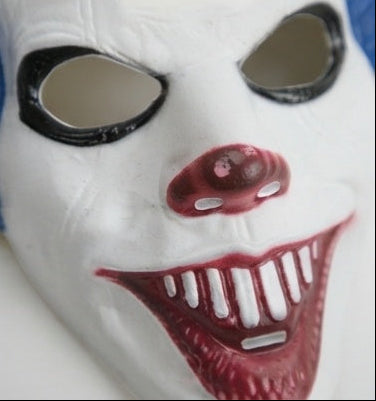 Close-up creepy clown face mask with blue hair, red mouth, black-lined eye holes