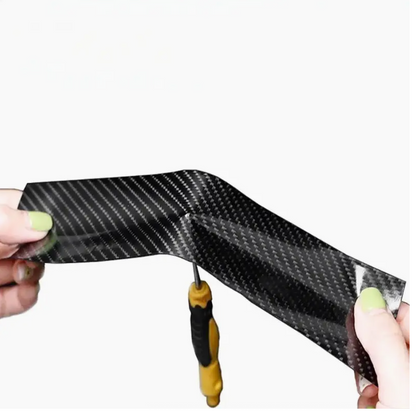 Hands trimming dark carbon fiber protection film strip for a curved surface