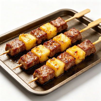 Baked meat and pineapple skewers on wooden sticks on a sheet tray