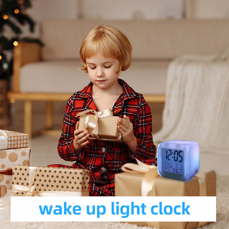 White cube LED alarm clock glowing on a tabletop beside a wrapped gift