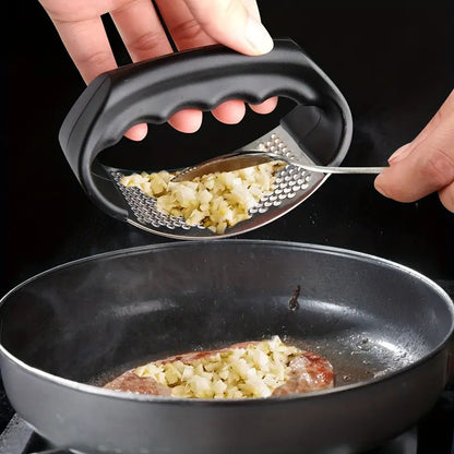Hand using black garlic press above a pan, minced garlic on the perforated plate