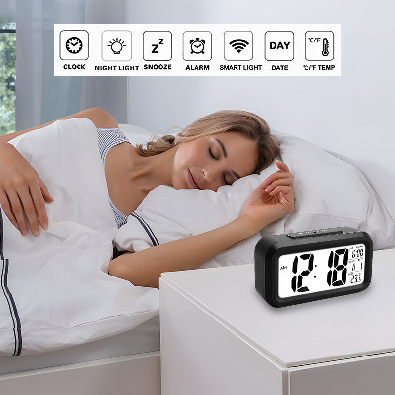 Black LED digital alarm clock beside the bed showing time and temperature in digital display