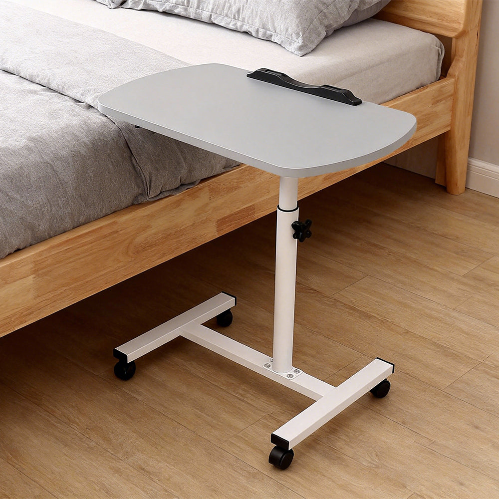 Adjustable overbed table tray with light grey top on wheeled white base, bedside setup