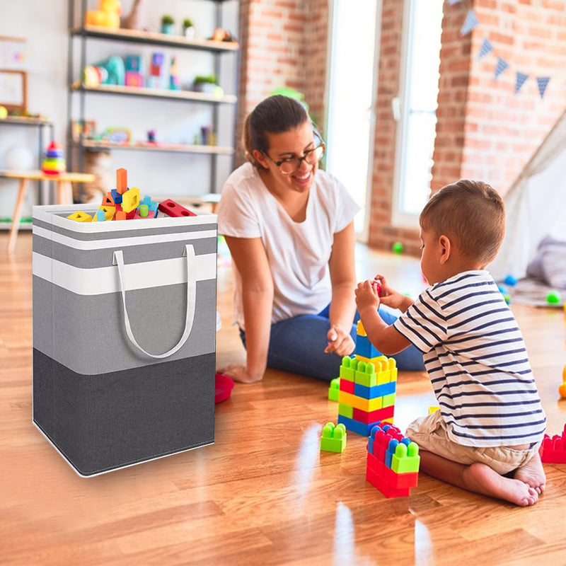 Grey folding laundry hamper bag with front handles beside toys in a living room