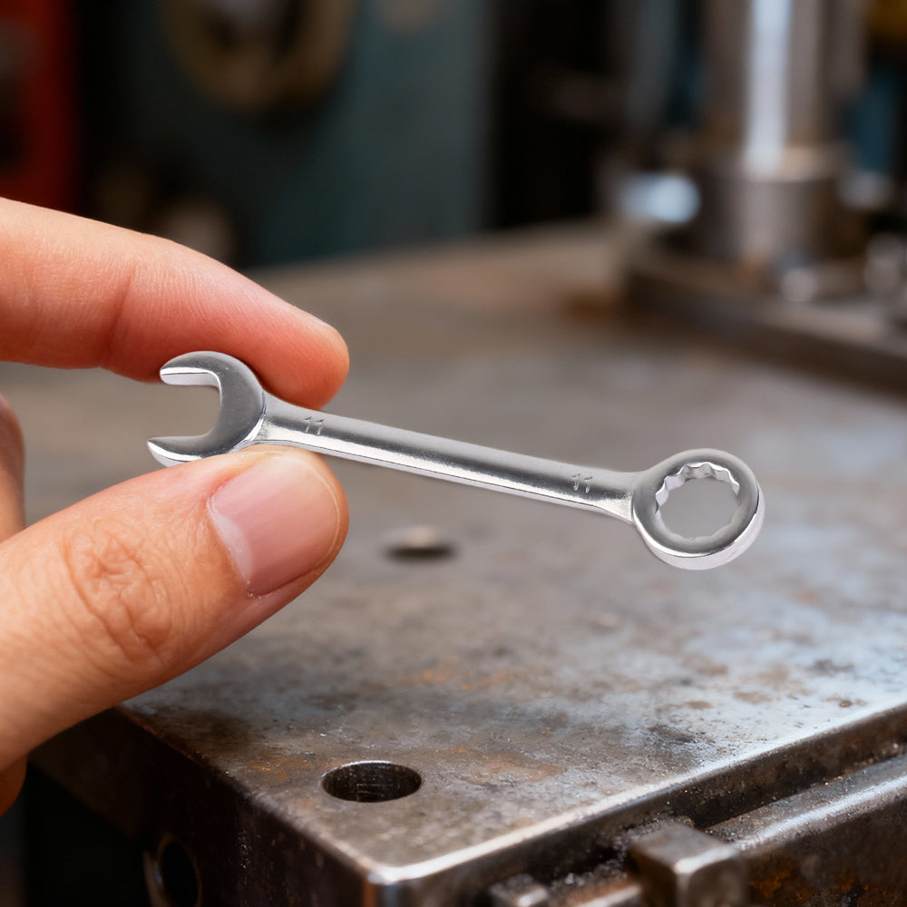 Mini combination wrench with open end and box end, held above a metal workbench