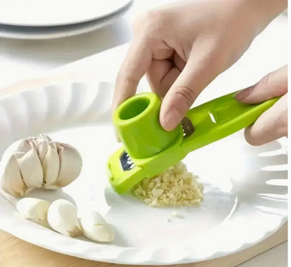 Green manual garlic press grinding garlic on a plate, cup pressed onto grater