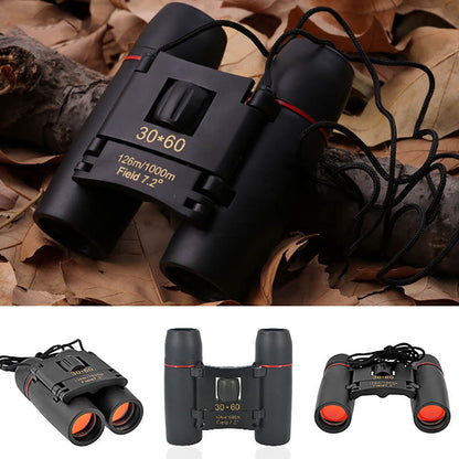 Black 30x60 binoculars with neck strap and eyepiece caps on leaves