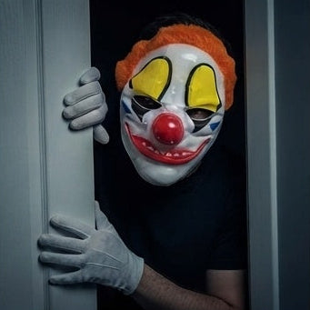 Clown mask with orange hair, yellow eyes, red nose, painted smile; grey-gloved hands