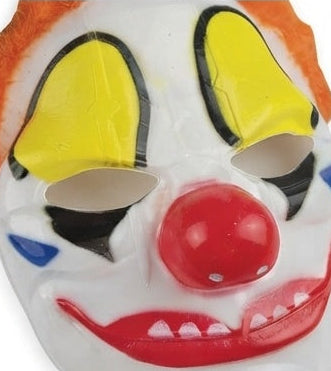 Clown mask close-up with orange hair, yellow eye shapes, red nose, and red grin