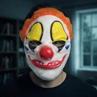 Clown mask worn on person with orange hair, yellow eyes, red nose, and wide painted smile